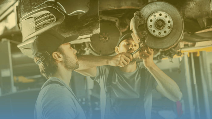one technician working on the brakes of a car while another technician watches